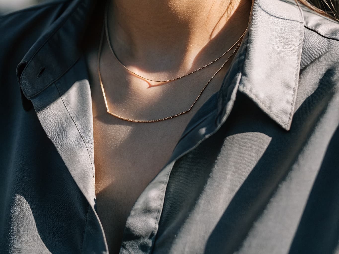 Thin discreet day collar chains worn under an open collared shirt, styled as everyday elegant jewelry